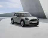 Mini Cooper 5 puertas en color gris claro, con llantas plateadas, estacionado en una zona de concreto con arquitectura moderna.