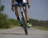 Kolarz w jaskrawozielonych butach i czarnych skarpetach, z nogami w pozycji do sprintu, osiąga tętno anaerobowe podczas jazdy po pustej drodze.