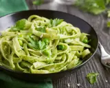 Pyszne tagliatelle z zielonym pesto, groszkiem i listkami pietruszki w czarnej misce.
