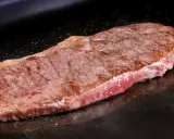 Un jugoso filete de ternera, recién hecho, con un borde dorado y un interior rosado, reposa sobre una plancha oscura.