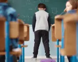 Chłopiec stoi przed tablicą z zadaniami matematycznymi.