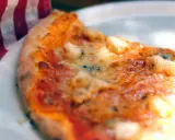 Tranche de pizza appétissante sur une assiette blanche, avec une serviette à carreaux rouges et blancs. Une recette parfaite avec de la farine sans gluten pour pizza.