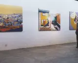 A person contemplates vibrant, stylized paintings in an art gallery, each piece curating meaning through bold colors and urban landscapes.