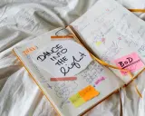 Carnet ouvert avec des notes manuscrites sur la création d'un livre, incluant "Dance into the Light" et des idées de marketing. Un nom d'auteur connu pourrait être inspiré par ces notes.