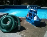 Un tuyau vert enroulé et une boîte bleue avec des accessoires de piscine, prêts pour le nettoyage. L'ordre des filtres à eau est essentiel pour une eau claire.