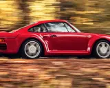 Czerwony Porsche 959 pędzi przez jesienny las, liście tworzą rozmyte smugi.