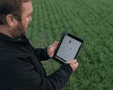 Farmer uses a tablet to monitor crop health and optimize yields, showcasing the power of digital farming in a lush green field.