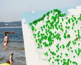 Ludzie kąpiący się w Bałtyku, obok mapa Polski z zaznaczonymi punktami, być może informującymi o zagrożeniu sinice bałtyk.