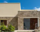 Moderne facciate in pietra grezza si alternano a intonaco chiaro, creando un contrasto materico. Un ingresso con porta in legno scuro e un giardino fiorito.