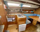 Cuisine de voilier avec cuisinière, évier double, banquette bleue et table en bois. Un radiateur est visible. 312 avis gib sea.