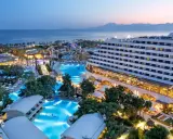 Luksusowy hotel Titanic Deluxe Lara z basenami i parkiem wodnym, oświetlony wieczorem, z widokiem na morze i góry.