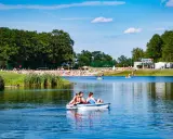Rodzina pływa rowerkiem wodnym po jeziorze na Dolnym Śląsku, w tle plaża pełna ludzi i zielone drzewa.