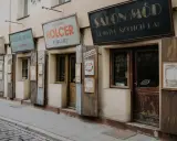 Ulica w dzielnicy żydowskiej Krakowa z zabytkowymi szyldami sklepów: "Salon Mód", "Benjamin Holcer Stolaz", "Stanisław Nowak Sklep Spożywczy".
