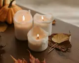 Candele accese su un tavolo di legno, con zucche e foglie autunnali. Un'ispirazione per chi vuole imparare come fare candele in casa.