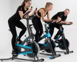 Trzy osoby ćwiczą na rowerach stacjonarnych. To świetny trening spinningowy!