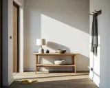 Minimalistyczna konsola w przedpokoju aranżacje: drewniany mebel z lampą, misą i ozdobnym kamieniem. Na ścianie wieszak z szalem.