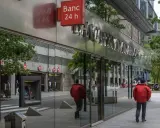 Un hombre con chaqueta roja camina por la acera frente a un edificio de **bpa finanzas** con un letrero de "Banc 24 h".