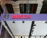 Logo Bosch i nazwa firmy na fioletowym tle. W tle widać instalacje przemysłowe, przewody i drabiny, sugerujące miejsce, gdzie odbywa się produkcja.