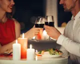 Romantyczna kolacja przy świecach. Para wznosi toast kieliszkami czerwonego wina, uśmiechając się do siebie.