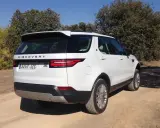 Un Land Rover Discovery HSE blanco aparcado en un camino de tierra rodeado de árboles.
