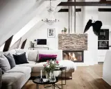 Mysigt vardagsrum med öppen spis, soffa och ett soffbord i 3 delar med blommor och ljus.