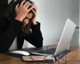Kobieta z rękami na głowie przy laptopie, symbolizująca wypalenie i decyzję o porzuceniu pracy.