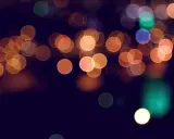 Rozmyte kule świateł, tworzące magiczny efekt bokeh w telefonie. Ciepłe pomarańcze i zielenie na ciemnym tle.