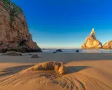 Goldene Sanddünen und Felsen am Praia da Ursa im warmen Abendlicht.