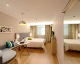 Habitación estrecha y alargada con cama, sofá curvo, mesa con portátil y espejo de cuerpo entero.