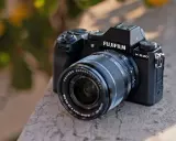 Czarny aparat Fujifilm X-S20 z obiektywem Fujinon leży na kamiennym murku.