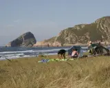 Gente en un playón de bayas, con carpas y sombrillas, disfrutando del mar y las montañas.