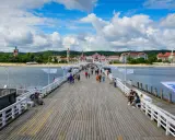 Spacer w Sopocie tętni życiem. Ludzie spacerują po drewnianym molo, podziwiając widok na plażę i zabytkowe budynki.