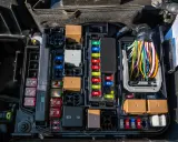 Caja de fusibles de coche con varios fusibles de diferentes amperajes y colores, relés marrones y un mazo de cables de colores.