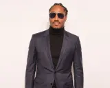 A man in a sharp black suit with a turtleneck, sporting stylish sunglasses.