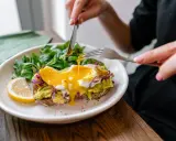 Tost z awokado i jajkiem sadzonym, polany żółtkiem, z sałatką i cytryną.