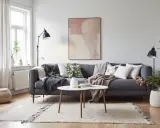 En grå soffa med många kuddar och filtar, ett runt soffbord och en matta skapar en mysig bohemisk inredning.