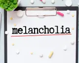 Na kartce widnieje napis "melancholia". Wokół leżą tabletki, strzykawka i maseczka, sugerując walkę z tym stanem.