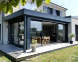 Une véranda moderne avec de grandes baies vitrées s'ouvre sur une terrasse en bois. La nouvelle loi sur les véranda permet de tels agrandissements.