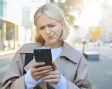 Zmarszczona kobieta patrzy na telefon, zastanawiając się, jak przestać zazdrościć innym.