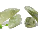 Cristalli grezzi di ametista verde, noti per il loro significato di crescita e rinnovamento, su sfondo bianco con foglie verdi.