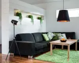 Ett modernt vardagsrum med mörk soffa, gröna kuddar och en träbord. Ljus och rum skapar en inbjudande atmosfär med växter i en nisch.