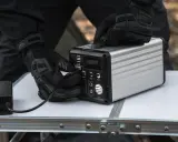 Ręce w rękawiczkach podłączają zasilacz do przenośnej stacji zasilania. To rozwiązanie pomoże Ci dowiedzieć się, jak zagotować wodę bez gazu i prądu.