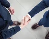 Dwaj mężczyźni w garniturach ściskają sobie dłonie na jasnej posadzce.