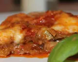 Deliciosa porción de parmigiana di melanzane, con capas de berenjena, salsa de tomate y queso fundido, adornada con una hoja de albahaca fresca.