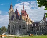 Imponujący zamek a pałac z kamienia, z wieżami i czerwonymi dachami, otoczony zielonym parkiem, gdzie odpoczywają ludzie.
