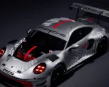 Silberner Porsche 911 GT3 R mit auffälligem Schachbrettmuster und roten Akzenten, bereit für die Rennstrecke.