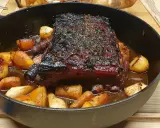 Poitrine de porc rôtie, croustillante et savoureuse, servie avec des pommes de terre et des carottes dans une cocotte en fonte.