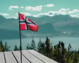 Norweska flaga na tle gór i jeziora. Pomyśl o tym, jak wysłać zwolnienie lekarskie do NAV, gdy jesteś w tak pięknych okolicznościach.