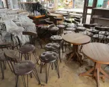 Viele gebrauchte Gastrostühle und runde Holztische stehen in einem Raum.