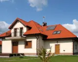 Nowoczesny dom z senioratką, z czerwonym dachem i panelami słonecznymi, otoczony zielonym trawnikiem.